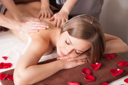 Young woman having massage in beauty spa by two therapistの写真素材