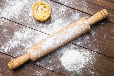 Wooden rolling pin with remnants of flour and pasta on old grainy textured wood surfaceの写真素材