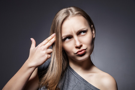 Depressed woman. Displeased young woman holding her hand like a gun near headの写真素材