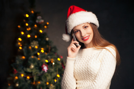 Young woman calling mobile in front of Christmas treeの写真素材
