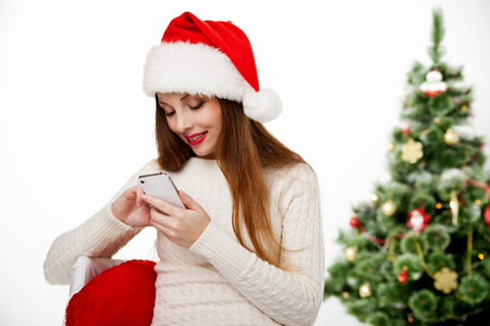Girl in santa hat call mobile phone by christmas tree Isolatedの写真素材