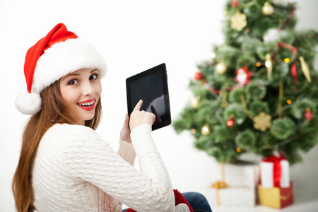 Happy woman sitting with tablet PC in front of Christmas tree isolatedの写真素材