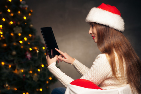 Happy woman sitting with tablet PC in front of Christmas treeの写真素材