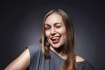 Young Happy Woman Sticking Out Her Tongue Over a Grey Backgroundの写真素材