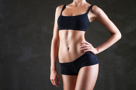 Slim tanned woman\'s body  over dark grey backgroundの写真素材
