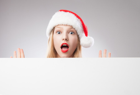 Joyful Beautiful christmas woman in santa hat holding empty board isolated on white backgroundの写真素材