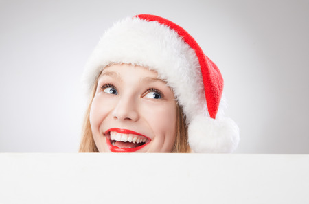Beautiful christmas woman in santa hat holding empty board and looking to the right isolated on white backgroundの写真素材