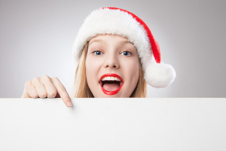 Beautiful christmas woman in santa hat pointing empty board, isolated on white backgroundの写真素材