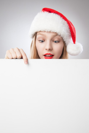 Beautiful christmas woman in santa hat pointing empty board, isolated on white backgroundの写真素材