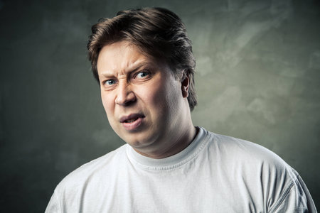 Man with disgusted expression over dark grey backgroundの写真素材
