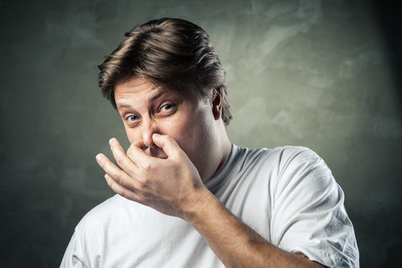 Man with disgusted expression closing his nostrils with his fingersの写真素材
