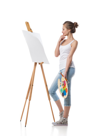 Thoughtful girl standing by canvas with a palette.Isolated.の写真素材