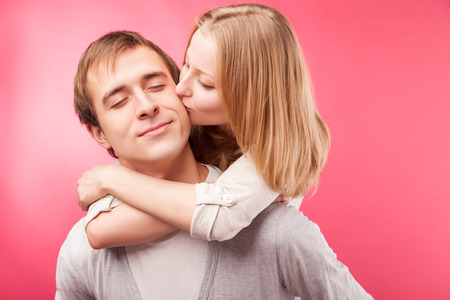 Teenage boy kissed by his girlfriend. Isolated over pink background.の写真素材