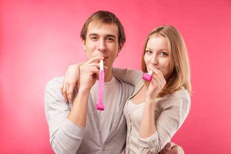love and family concept - smiling couple with whistles hugging, looking in the camera. Isolated over pink background.の写真素材