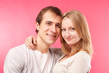love and family concept - smiling couple hugging, looking in the camera. Isolated over pink background.の写真素材