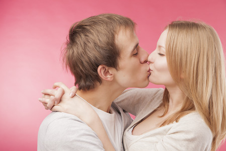 Close up studio portrait of young boy kissing cute girlfriend. Isolated on pink background.の写真素材