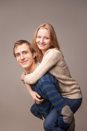 Portrait of a young couple, the girl is on her boys back. Isolated over brown background.の写真素材