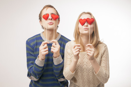 Young couple hiding their lips behind  little red hearts. Isolated over pink background.の写真素材
