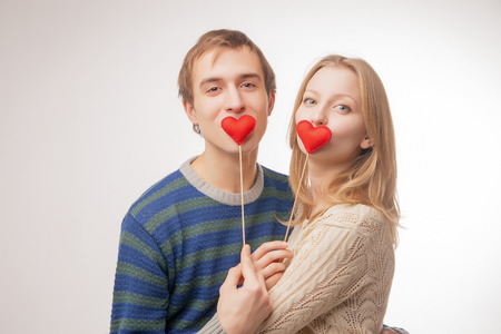Young couple hiding their lips behind  little red hearts. Isolated over pink background.の写真素材