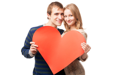 young smiling couple holding sign in form of red heart, heads close, isolated on white backgroundの写真素材