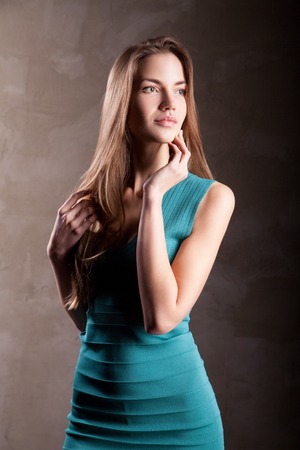 Portrait of attractive fashion girl in turquoise dress looking away, isolated over dark background.の写真素材