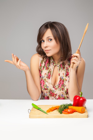 Thoughtful  young woman chopping vegetables  over the gray background.の写真素材