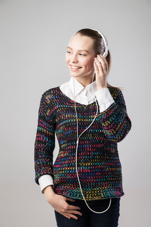 Smiling woman with headphones listening to music on player and looking aside. Music teenager girl portrait against isolated grey backgroundの写真素材