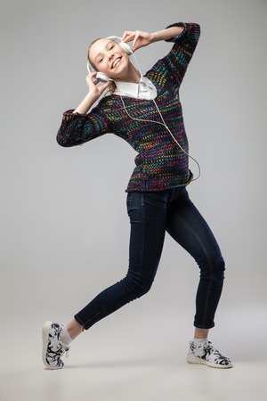 Girl With Headphones Singing and Dancing  leaning back. On grey Background. Full length portrait.の写真素材