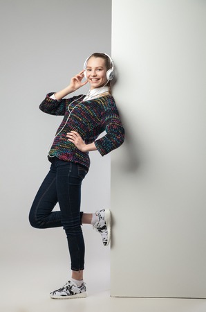 Young relaxed woman leaning on wall listening to music with headphones.Full length portrait.の写真素材