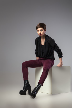 beautiful thin brunette woman  sitting her legs apart on cube over gray backgroundの写真素材
