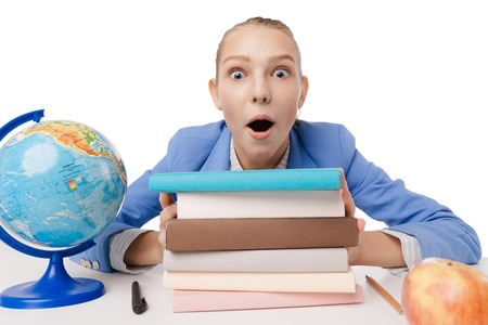 Closeup portrait shocked, surprised overwhelmed student sitting at desk in front pile books, studying, cant believe her eyes isolated over white background. Education. Face expressionの写真素材