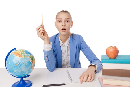 Surprised girl with red pencil sitting at table with a notebook and a stack of books. Isolated over white background.の写真素材