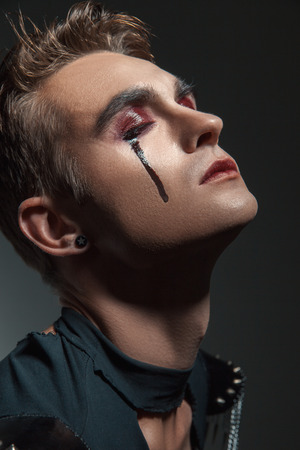 a young man  with  make  up and painted tears. his eyes closed. Isolated.の写真素材