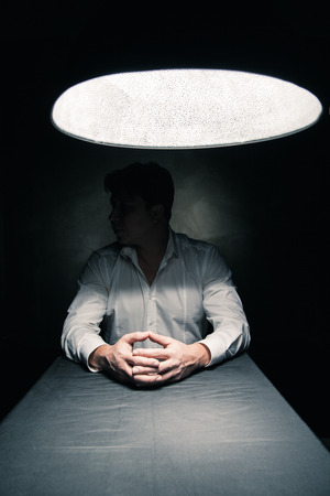 Man in a dark room illuminated only by a light coming from a lamp no face seenの写真素材