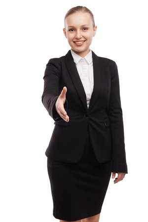 Closeupof confident young businesswoman in suit stretching out hand for shaking and smiling while standing against white backgroundの写真素材