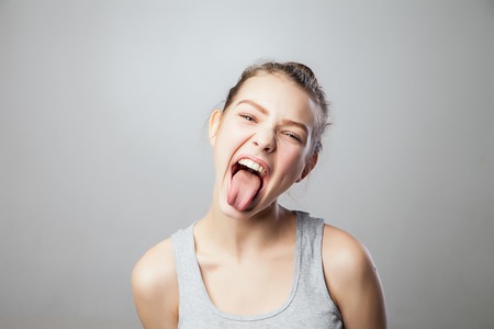 Young pretty woman shoots out tongue, isolated on greyの写真素材