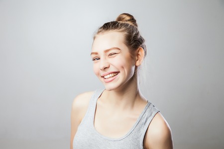 Closeup of a beautiful young woman winking. Isolated over grey background.の写真素材