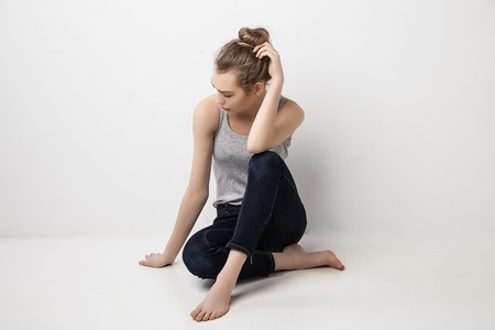 Beautiful melancholic girl sitting on the floor and looking down. Isolated over grey background.の写真素材