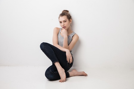 Beautiful melancholic girl sitting on the floor . Isolated over grey background.の写真素材