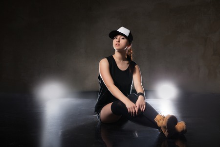 Sexy young woman in a trendy clothes sitting one one leg over black backgroundの写真素材