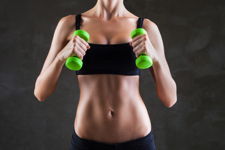 Body of young fit woman lifting dumbbells over dark grey backgroundの写真素材