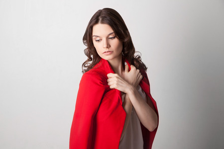 Young beautiful woman holding red jacket on a shoulders. Looking downの写真素材