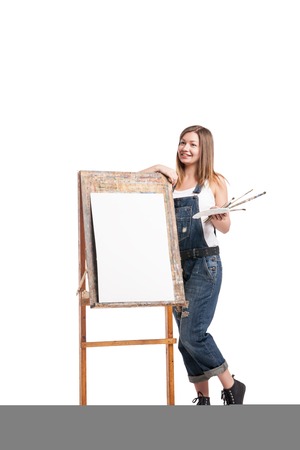 Smiling woman painter with paintbrush standing at easelの写真素材