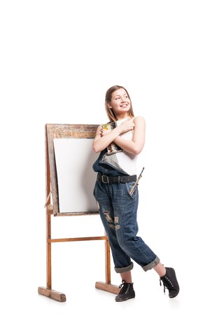 Smiling woman painter with paintbrush standing at easel , hugging paletteの写真素材