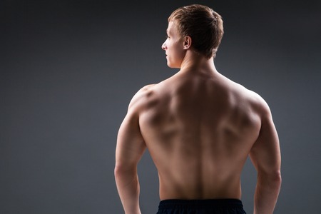 Muscular young man in studio on dark background shows the different movements and body parts. Back viewの写真素材