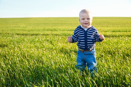 Beautiful baby boy standing in the green grass on spring fieldの写真素材