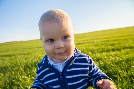 Beautiful baby boy standing in the green grass on spring fieldの写真素材