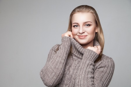 Beautiful blond young girl wears winter pullover over gray backgroundの写真素材
