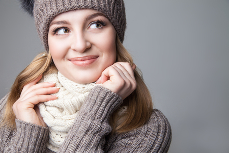 Beautiful blond young girl wears winter scarf and hat over gray backgroundの写真素材
