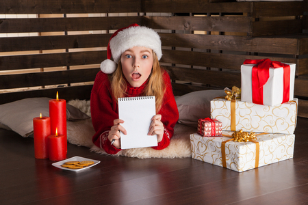 Happy young girl with Christmas presents laying on wooden floor whiting letter to Santaの写真素材